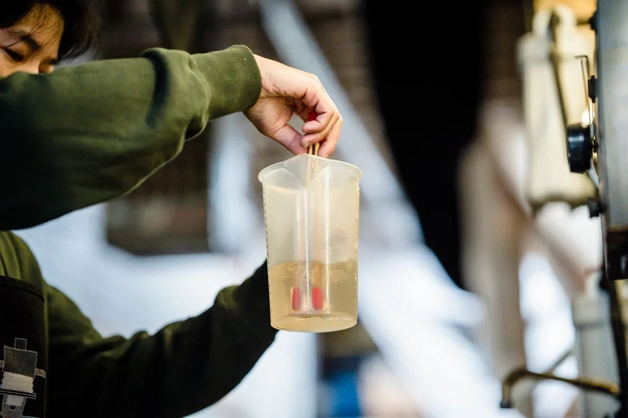 Hand houdt een maatbeker vast met een dichtheidsmeter in een troebele vloeistof