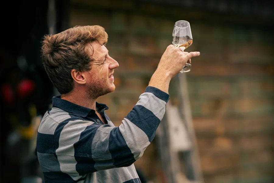 Wijnmaker houdt een glas witte wijn tegen het licht in een kelder